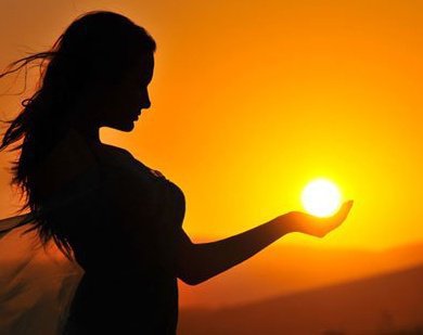 Silhouette of woman holding sun at sunset